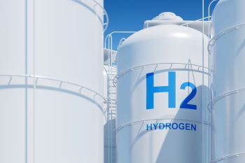 Two white storage tanks labeled "H2" and "HYDROGEN" against a clear blue sky.