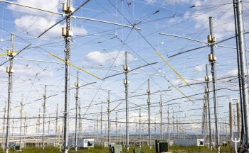 An array of tall antennas and intricate wiring under a blue sky with scattered clouds.