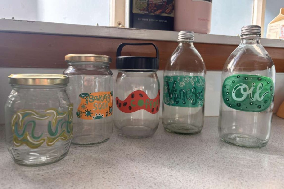 A collection of five labeled glass jars on a countertop, decorated for storing baking soda, coffee, vinegar, and oil.