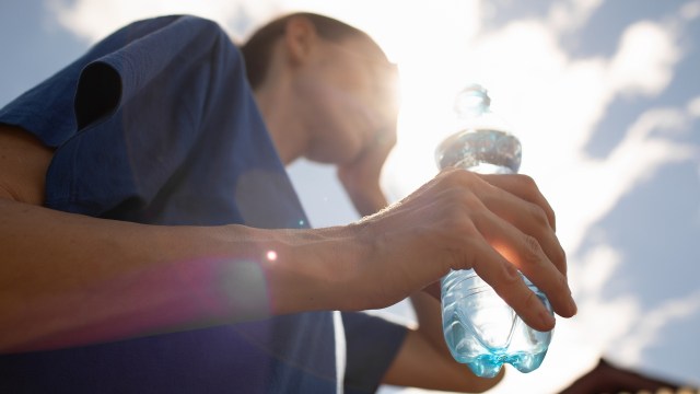 A person holding a water bottle while squinting against bright sunlight.