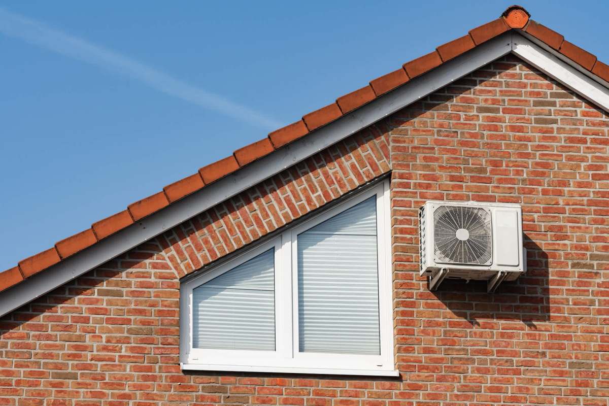 A brick house with a triangular window and an air conditioning unit on the exterior wall.