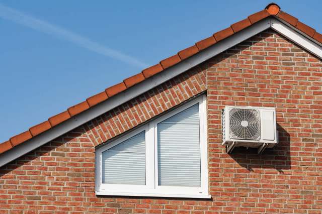 A brick house with a triangular window and an air conditioning unit on the exterior wall.