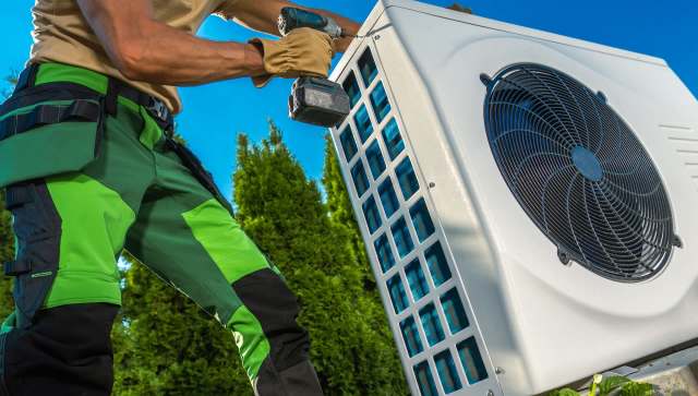 A technician is installing an air conditioning unit in a residential area on a sunny day.