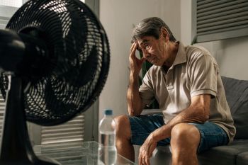 An elderly person sits in front of a fan in a heat wave.