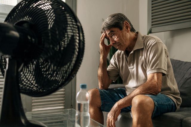 An elderly person sits in front of a fan in a heat wave.