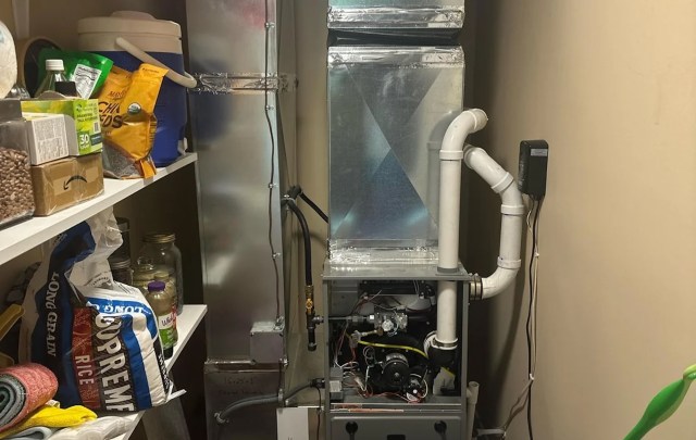 A furnace is installed in a utility space next to shelves filled with food items and storage containers.