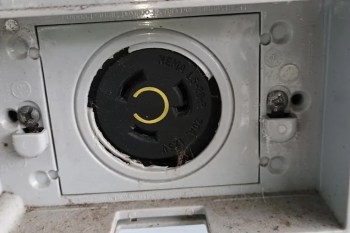 A close-up of a weathered electrical outlet with a black circular cover and visible dust and spider webs.