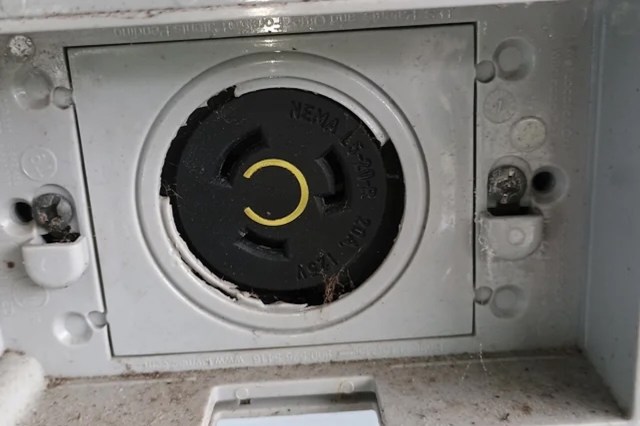 A close-up of a weathered electrical outlet with a black circular cover and visible dust and spider webs.