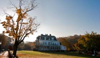 A historic white mansion surrounded by colorful autumn trees under a clear blue sky.