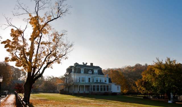 A historic white mansion surrounded by colorful autumn trees under a clear blue sky.