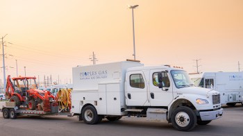 A white truck from Peoples Gas carries a trailer with construction equipment and tools in a parking area.