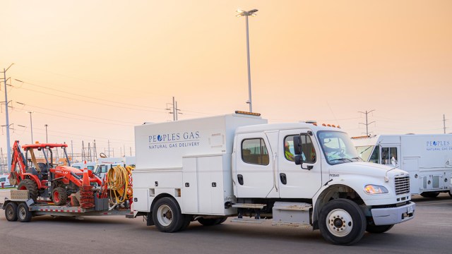 A white truck from Peoples Gas carries a trailer with construction equipment and tools in a parking area.