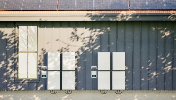 A modern home exterior featuring solar panels and two energy storage units on a grey wall.
