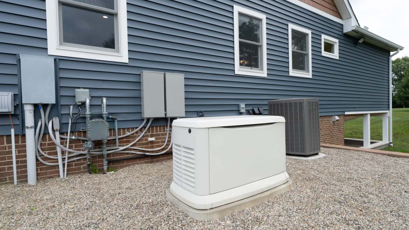 A residential exterior featuring a generator and utility boxes beside a blue siding house on gravel.