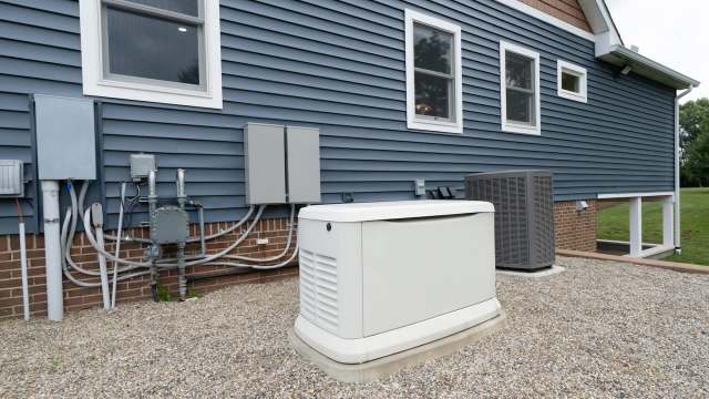 A residential exterior featuring a generator and utility boxes beside a blue siding house on gravel.