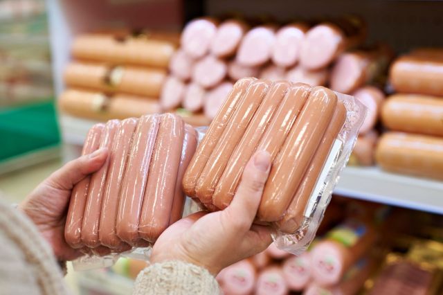 A person holding two packages of hotdogs.