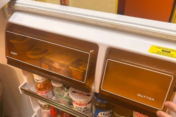 A close-up of a refrigerator shelf showing dairy and butter compartments with various condiments below.
