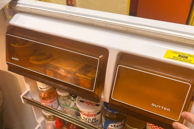A close-up of a refrigerator shelf showing dairy and butter compartments with various condiments below.