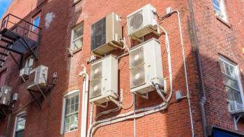 An exterior brick wall featuring multiple air conditioning units and exposed piping.