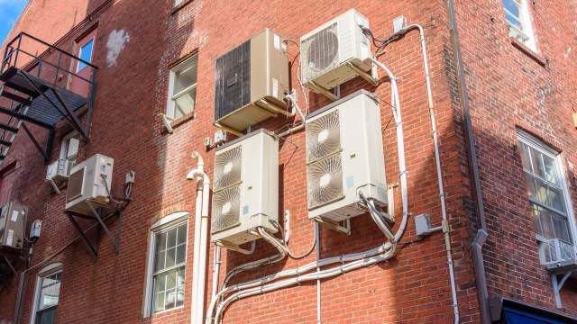 An exterior brick wall featuring multiple air conditioning units and exposed piping.