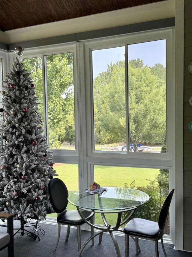Sliding floor-to-ceiling windows in a home overlooking a yard on a sunny day.