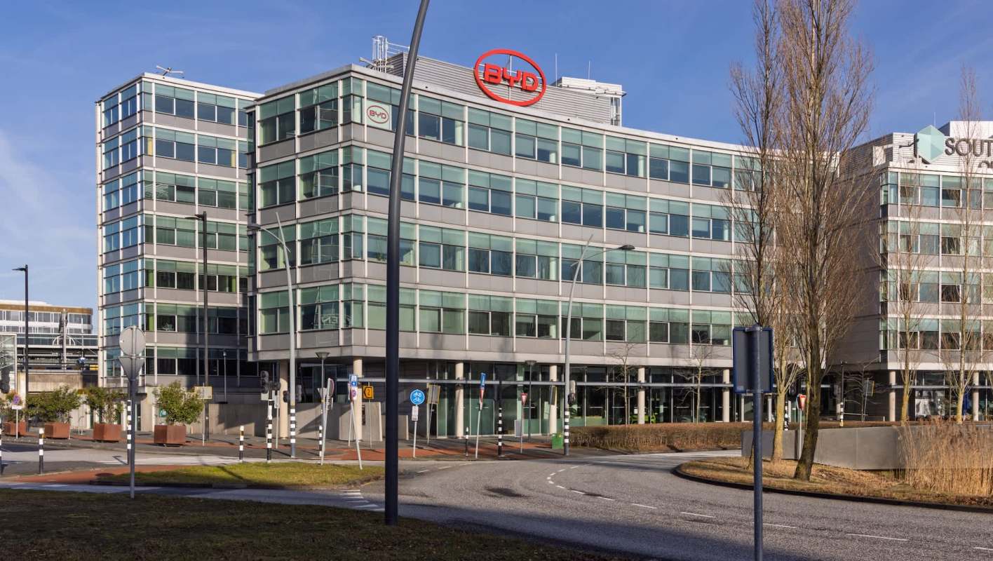 A modern office building with large glass windows and signage for BYD, surrounded by a landscaped area.