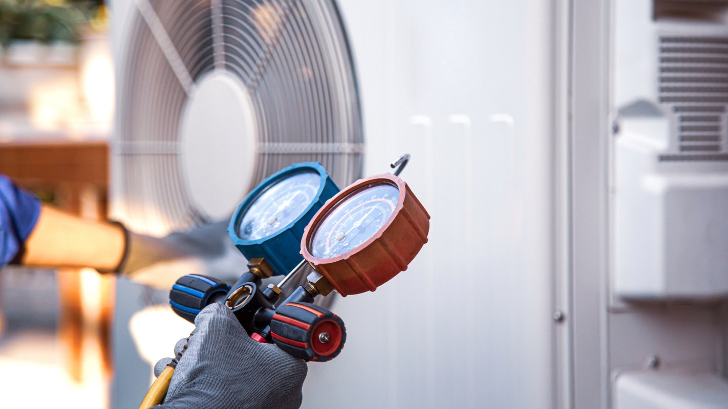 A technician holding a pressure gauge and inspecting an HVAC.