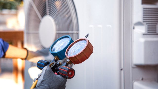A technician holding a pressure gauge and inspecting an HVAC.