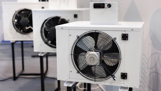 Three air conditioning units are displayed on stands, featuring visible fans and control panels.