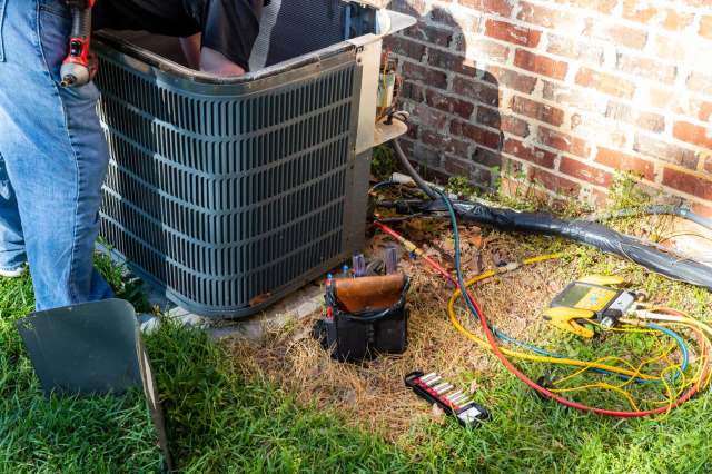 A person working to repair an outdoor AC unit.