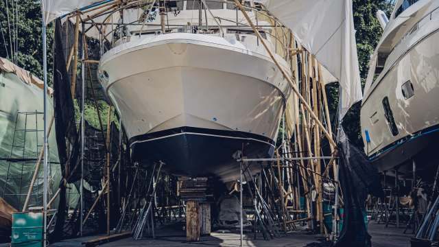 A yacht on stilts in a boatyard surrounded by scaffolding and tarpaulins.