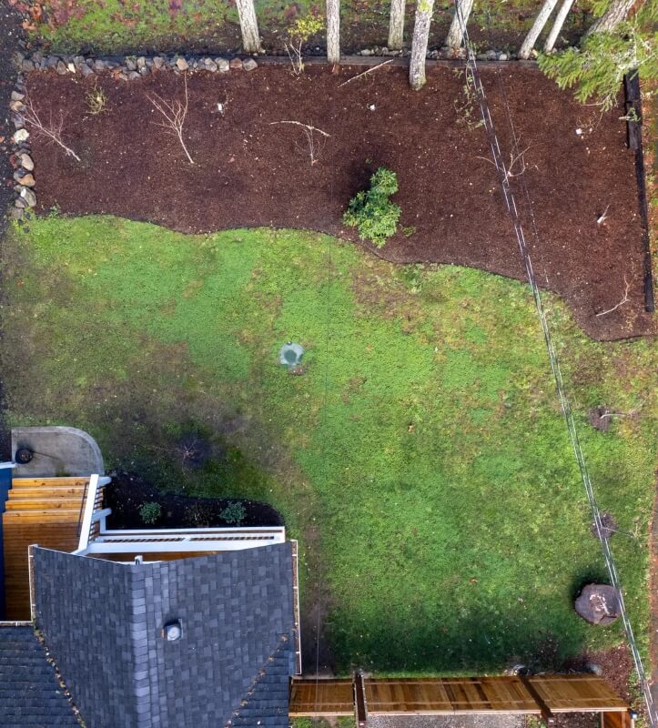 An overhead view of a garden showing a big lawn and large, empty flowerbed.