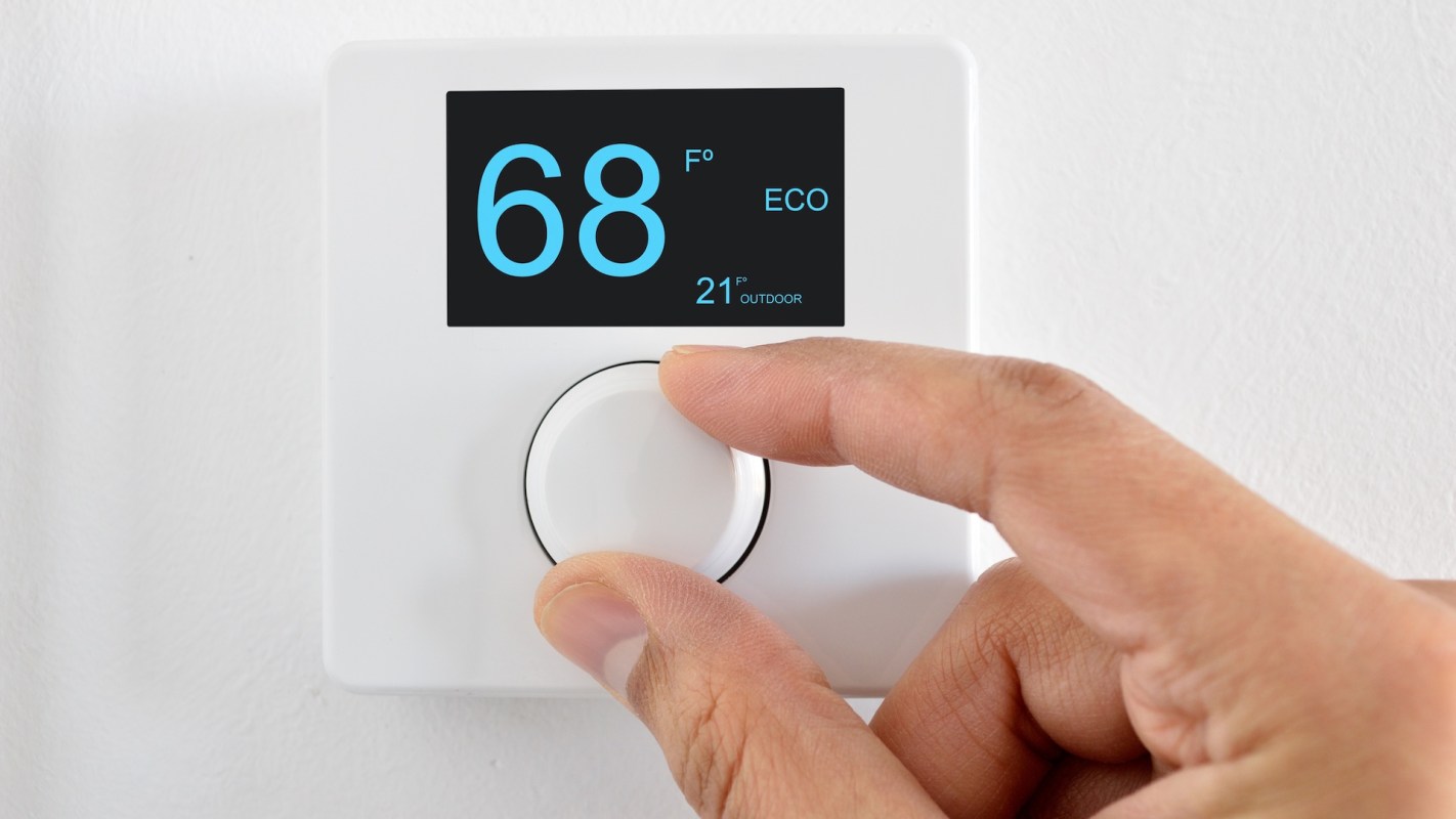 A hand adjusting a smart thermostat displaying a temperature of 68°F.