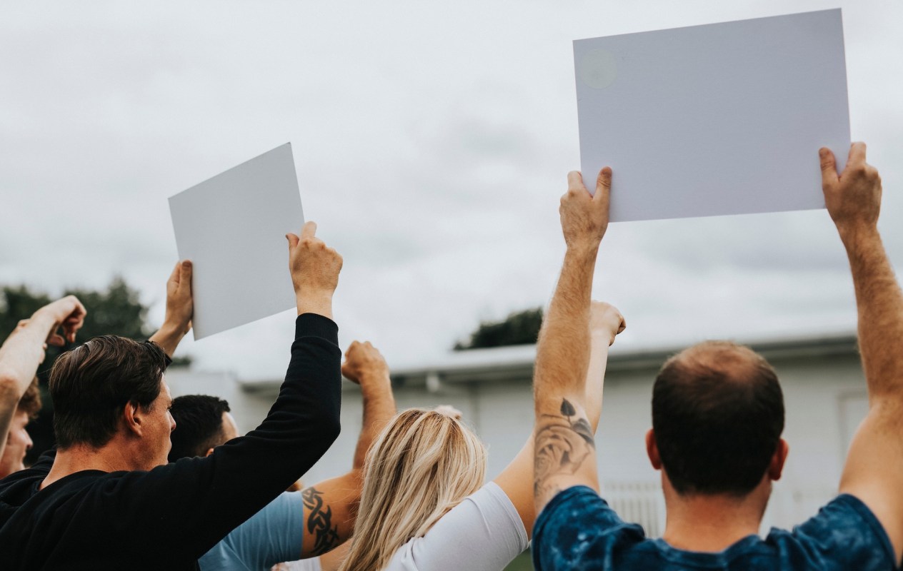 A group of people raising blank signs in the air during a protest or demonstration.