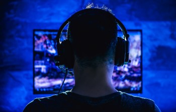 A person wearing headphones is focused on a computer screen illuminated by blue light.