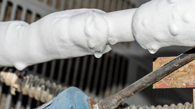 Foam covers a pipe with a droplet forming, set against a background of metal components.