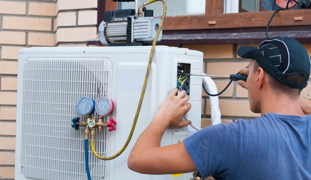 A technician repairs an air conditioning unit using tools and checking pressure gauges attached to the system.