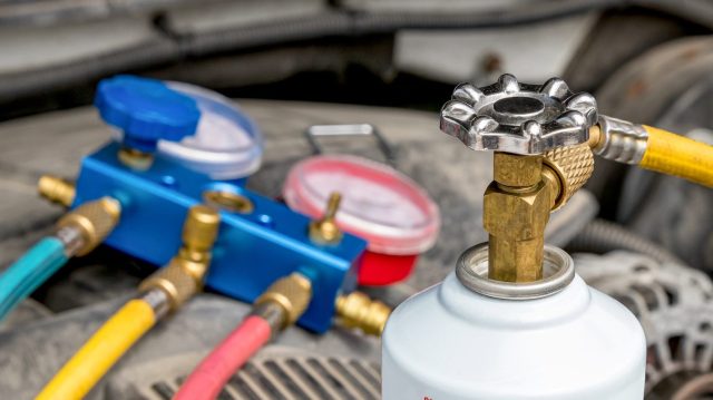 A refrigerant canister connected to a manifold gauge set in an automotive engine compartment.