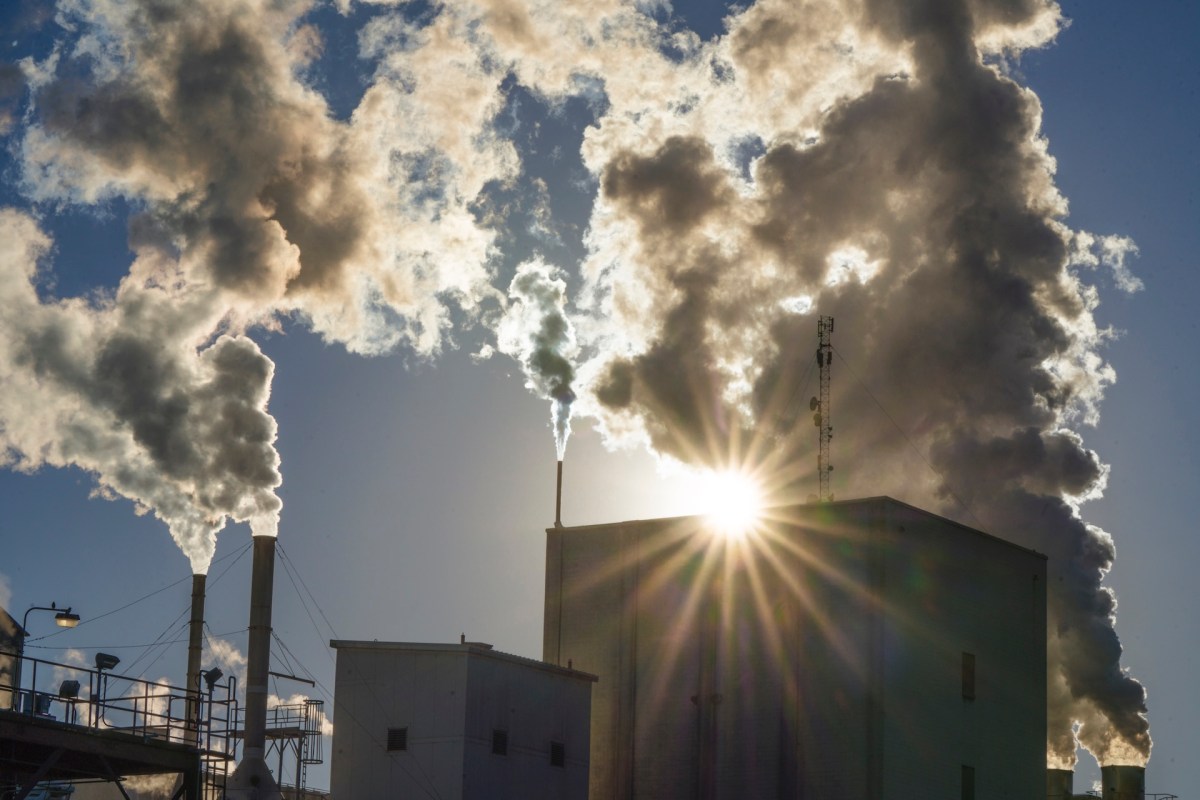 A factory emitting thick clouds of steam and smoke against a backdrop of sunlit clouds.