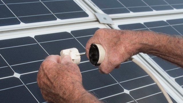 A person connects an electrical plug to a solar panel, showcasing renewable energy technology.