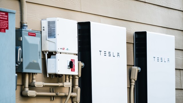 Two Tesla Powerwall batteries mounted on a wall beside a generation panel and connected pipes.