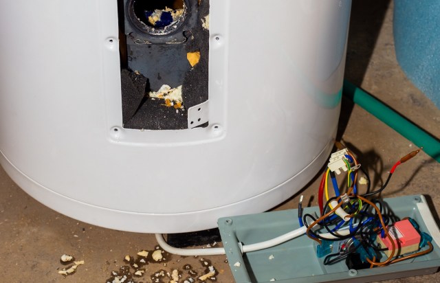 A damaged water heater with exposed wiring and debris scattered on the floor.
