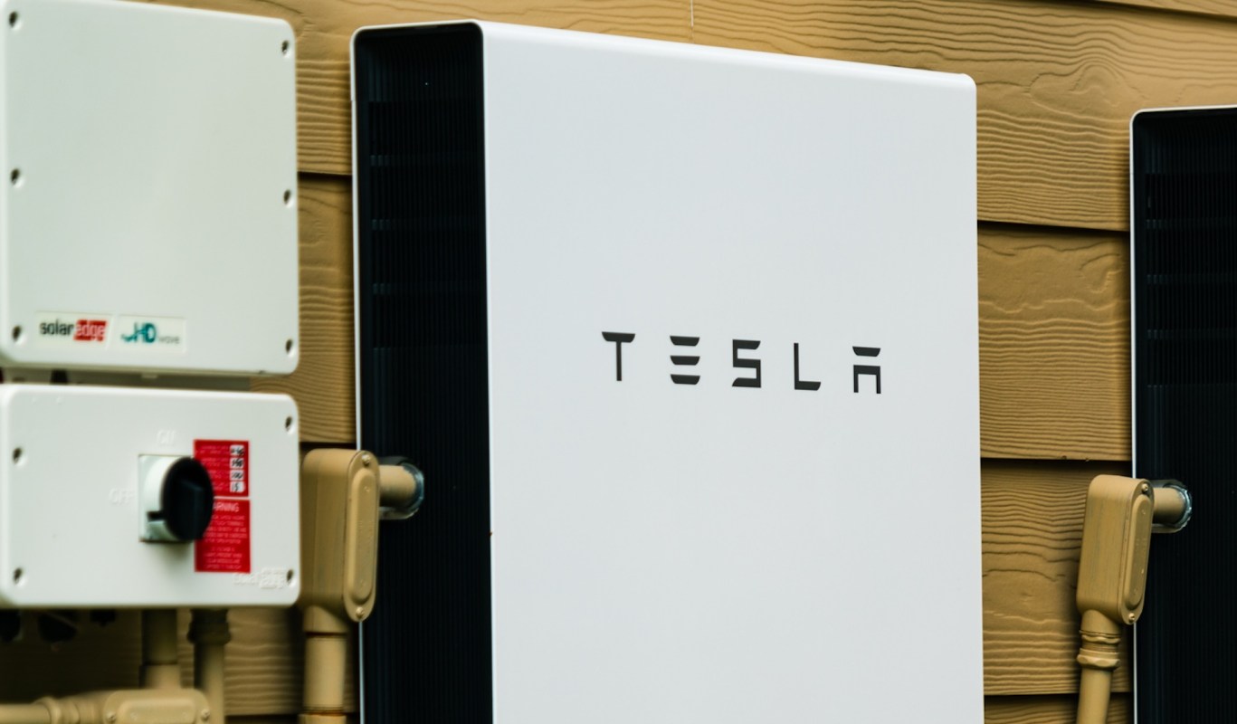 A Tesla Powerwall energy storage unit mounted on a wall beside solar power equipment.