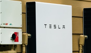 A Tesla Powerwall energy storage unit mounted on a wall beside solar power equipment.