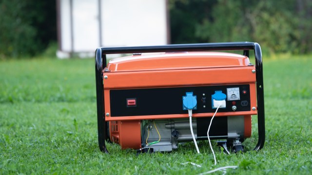 A portable orange generator sits on green grass with visible power outlets and a voltage meter.