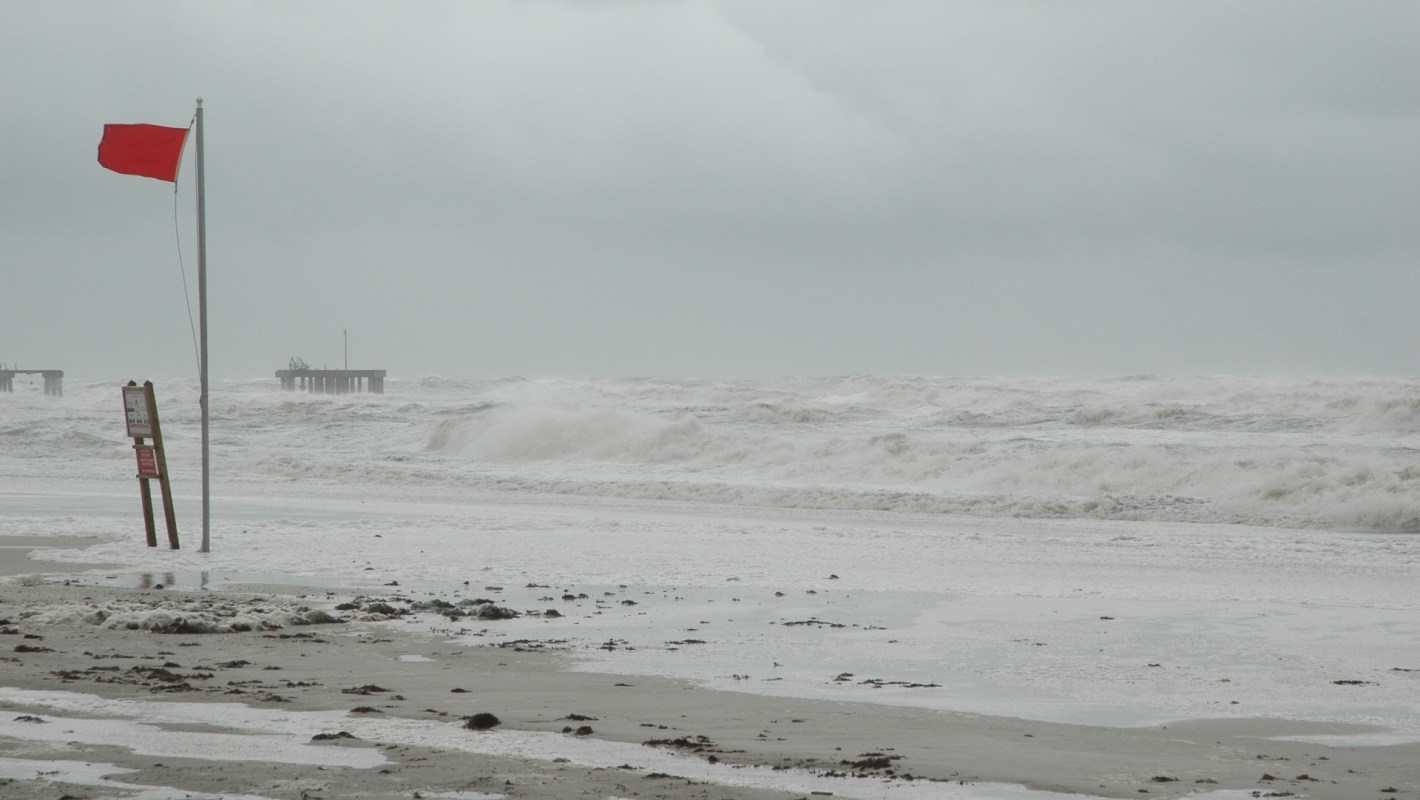 A stormy beach with a red flag hurricane warning.