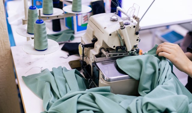 A sewing machine with a person's hand working on green fabric surrounded by spools of thread.