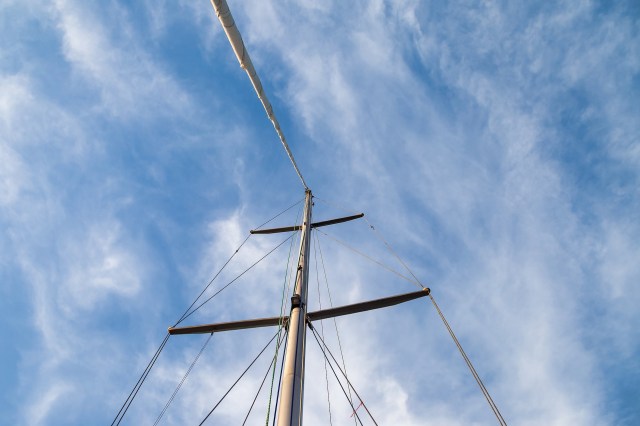 A view looking up at a sailing mast against a blue sky with wispy clouds.