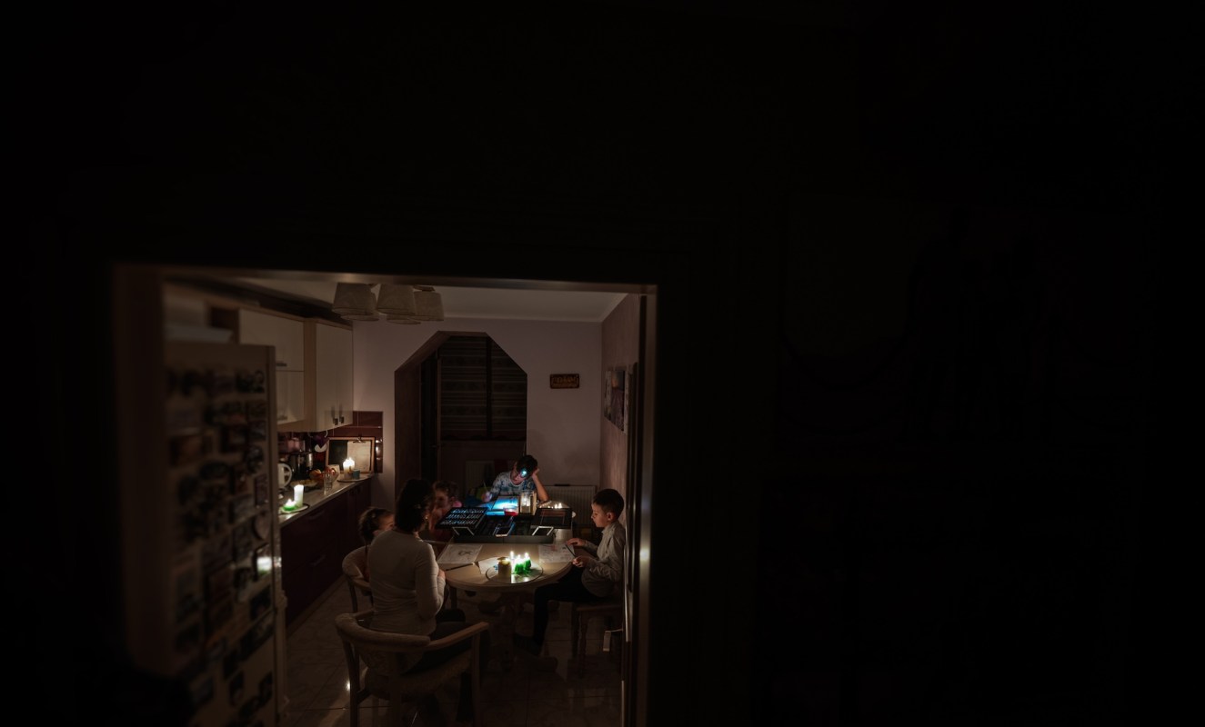 A family gathers around a table during a blackout, engaged in various activities with candles illuminating the space.