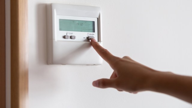 A person pressing the "ON/OFF" button of a digital thermostat.